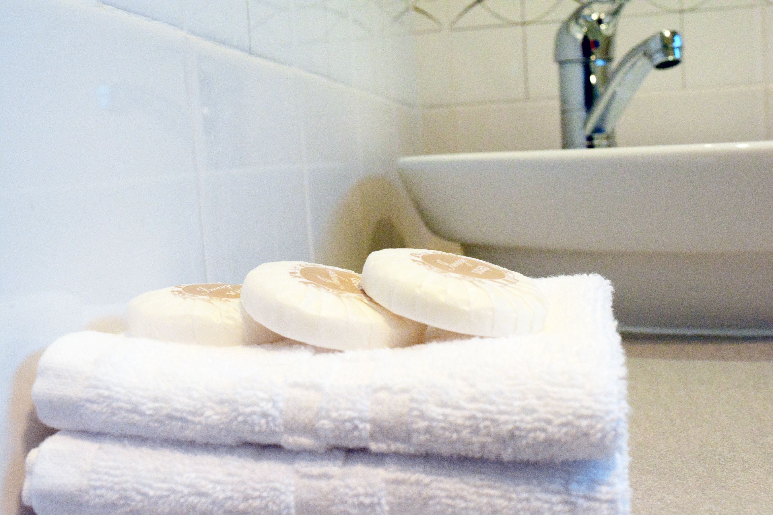 Una pila de toallas blancas y dos jabones sobre una encimera de baño.