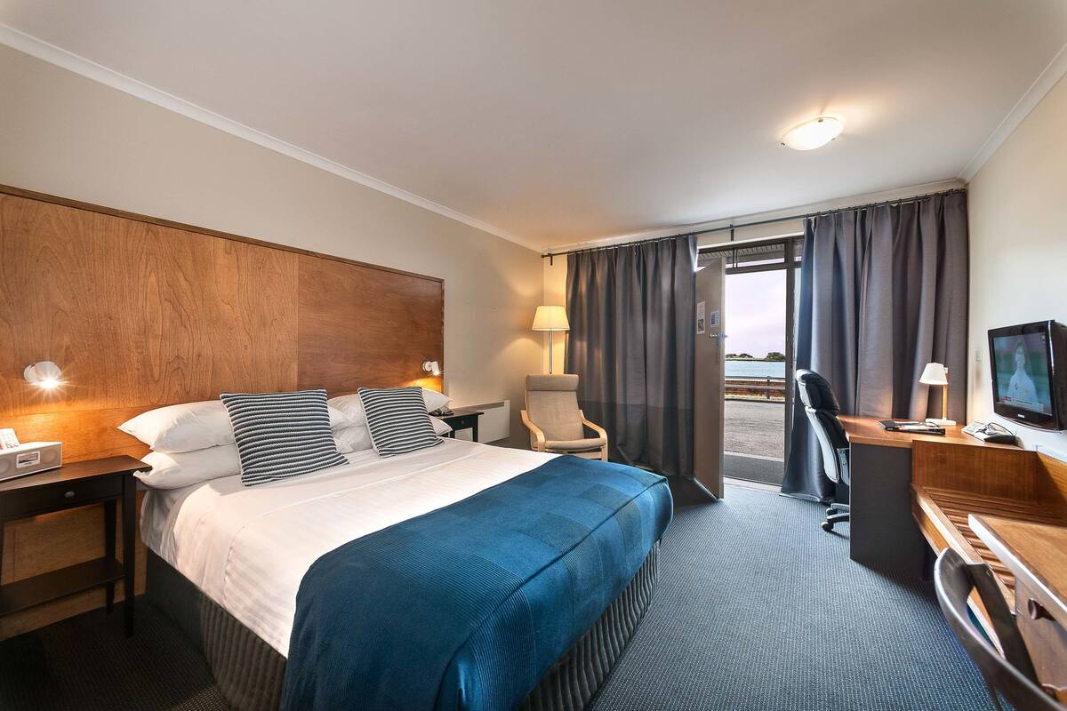 Habitación de hotel con una cama grande, un escritorio, una silla, un televisor y vistas al exterior.