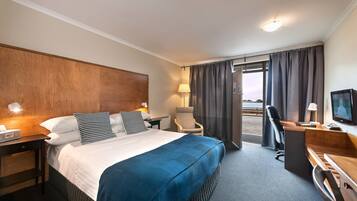 A hotel room with a large bed, a desk, a chair, a television, and a view of the outdoors.