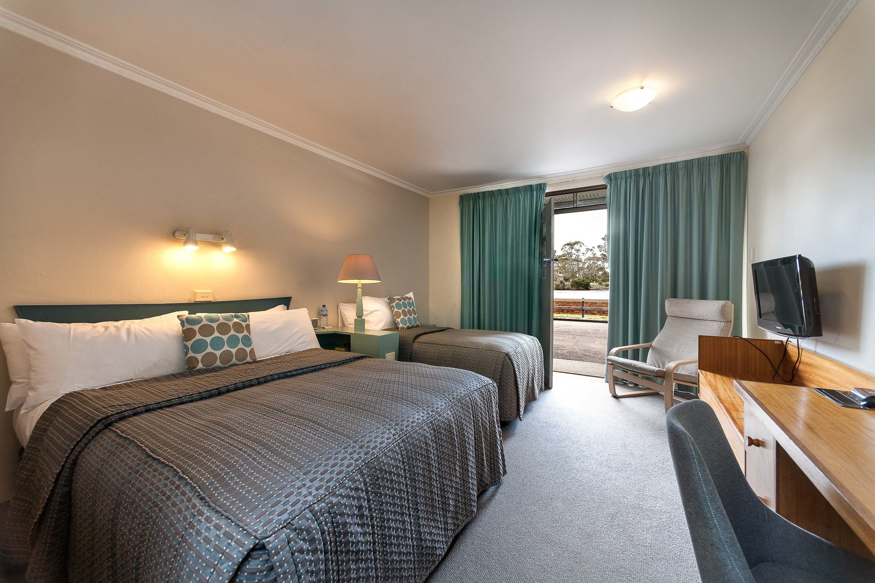 A hotel room with two beds, a desk, a chair, a TV, and a window with curtains.
