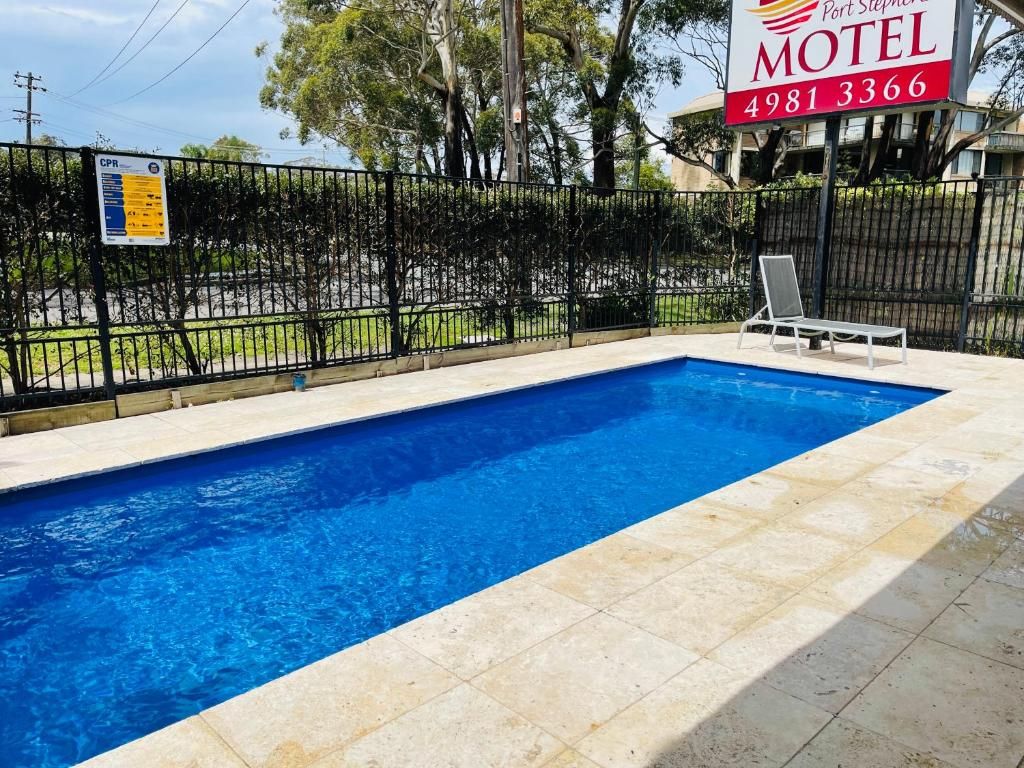 A swimming pool with a tiled edge, a lounge chair, and a fence.