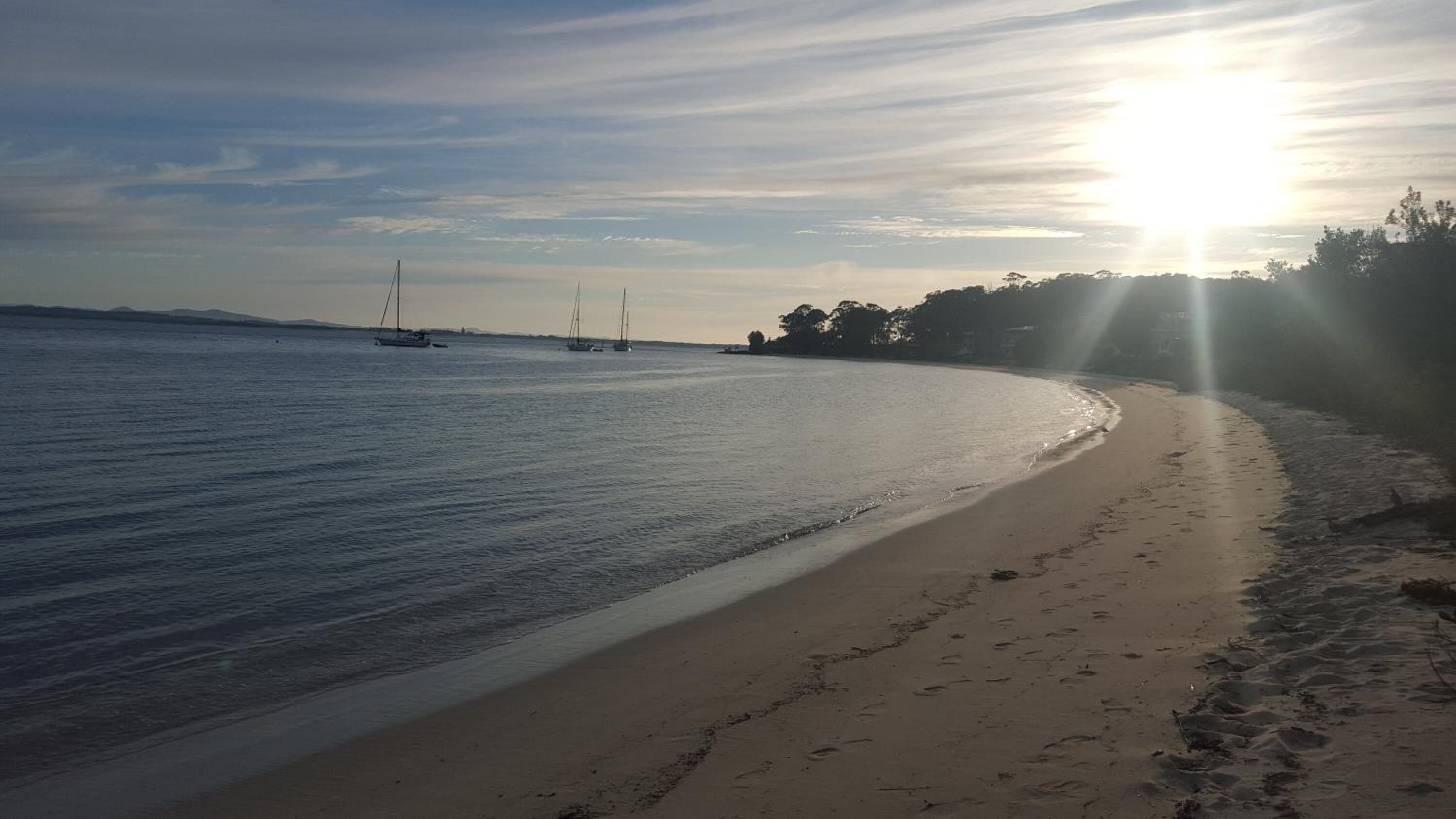 Ein Strand mit ruhigem Wasser, blauem Himmel und ein paar Segelbooten in der Ferne.