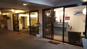 L’entrée d’un hôtel, avec un comptoir de réception, une pancarte « Bienvenue » et une autre indiquant « Entrez, nous sommes ouverts ».