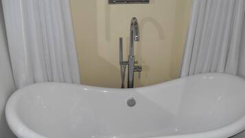A white freestanding bathtub in a bathroom with beige walls and white curtains.