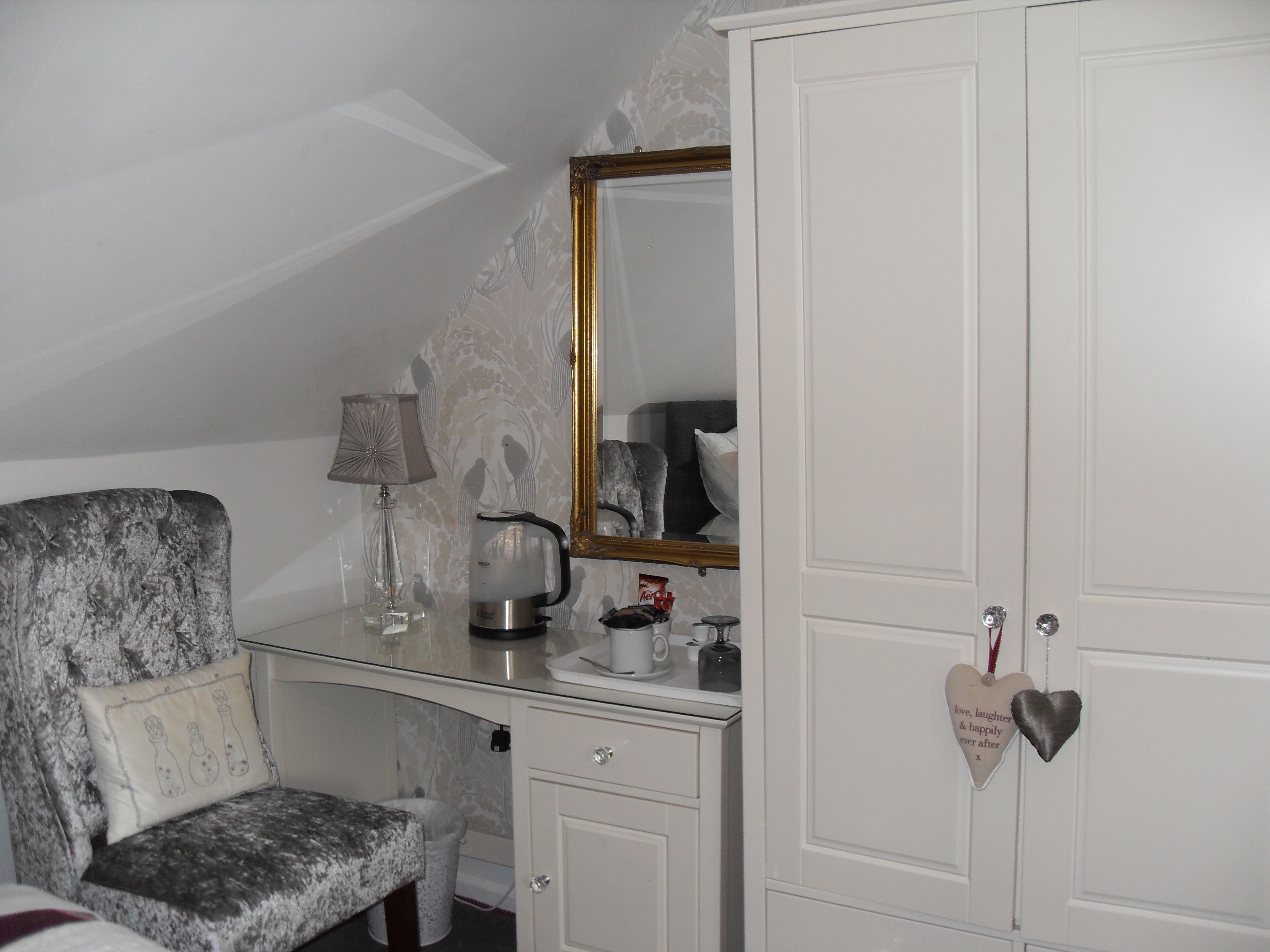 A bedroom with a bed, a dresser, a mirror, and a desk with a lamp and a kettle.