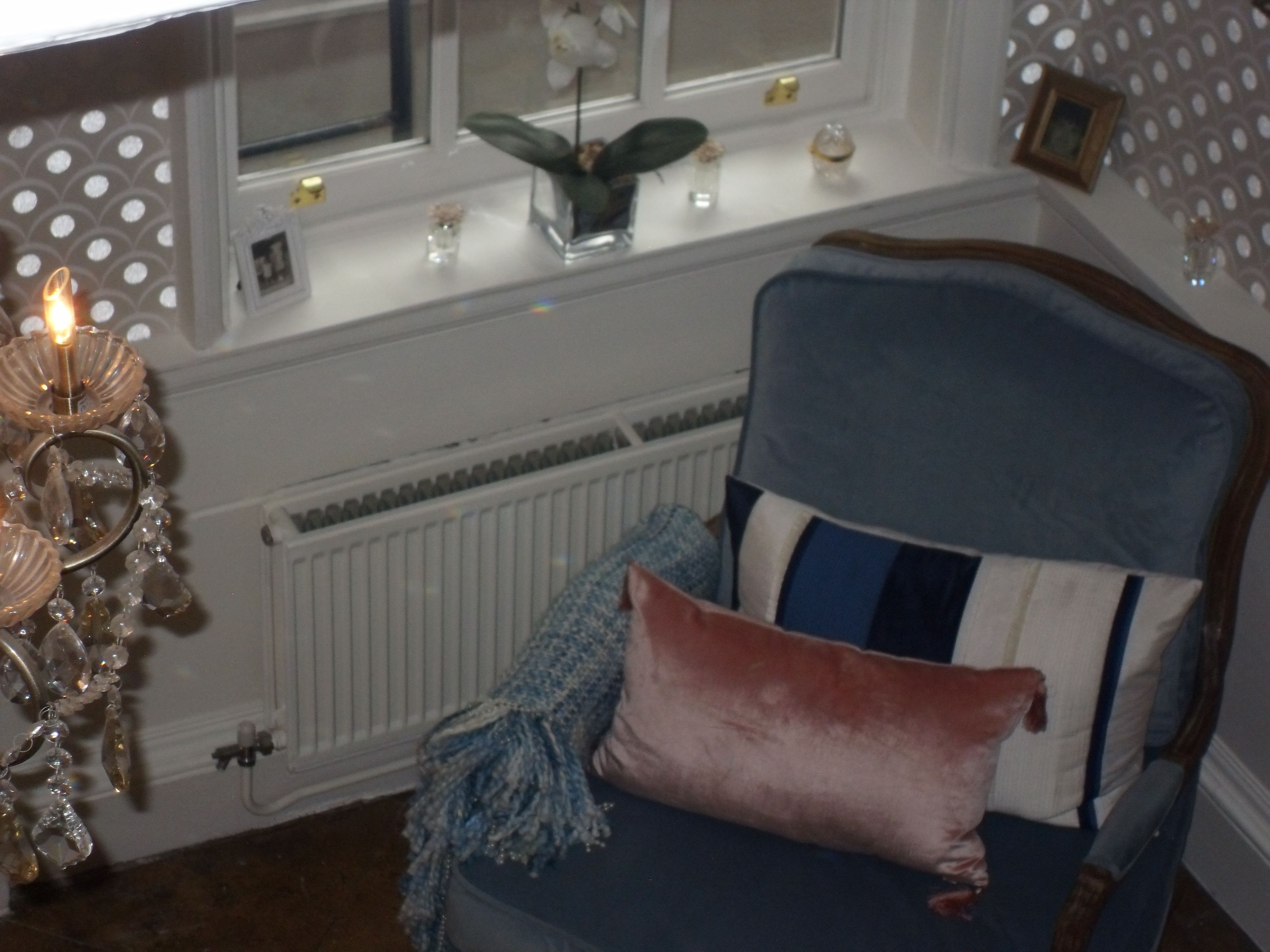 Une pièce avec un fauteuil bleu, un lustre décoratif et une fenêtre donnant sur l’extérieur.