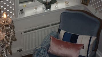 Une pièce avec un fauteuil bleu, un lustre décoratif et une fenêtre donnant sur l’extérieur.