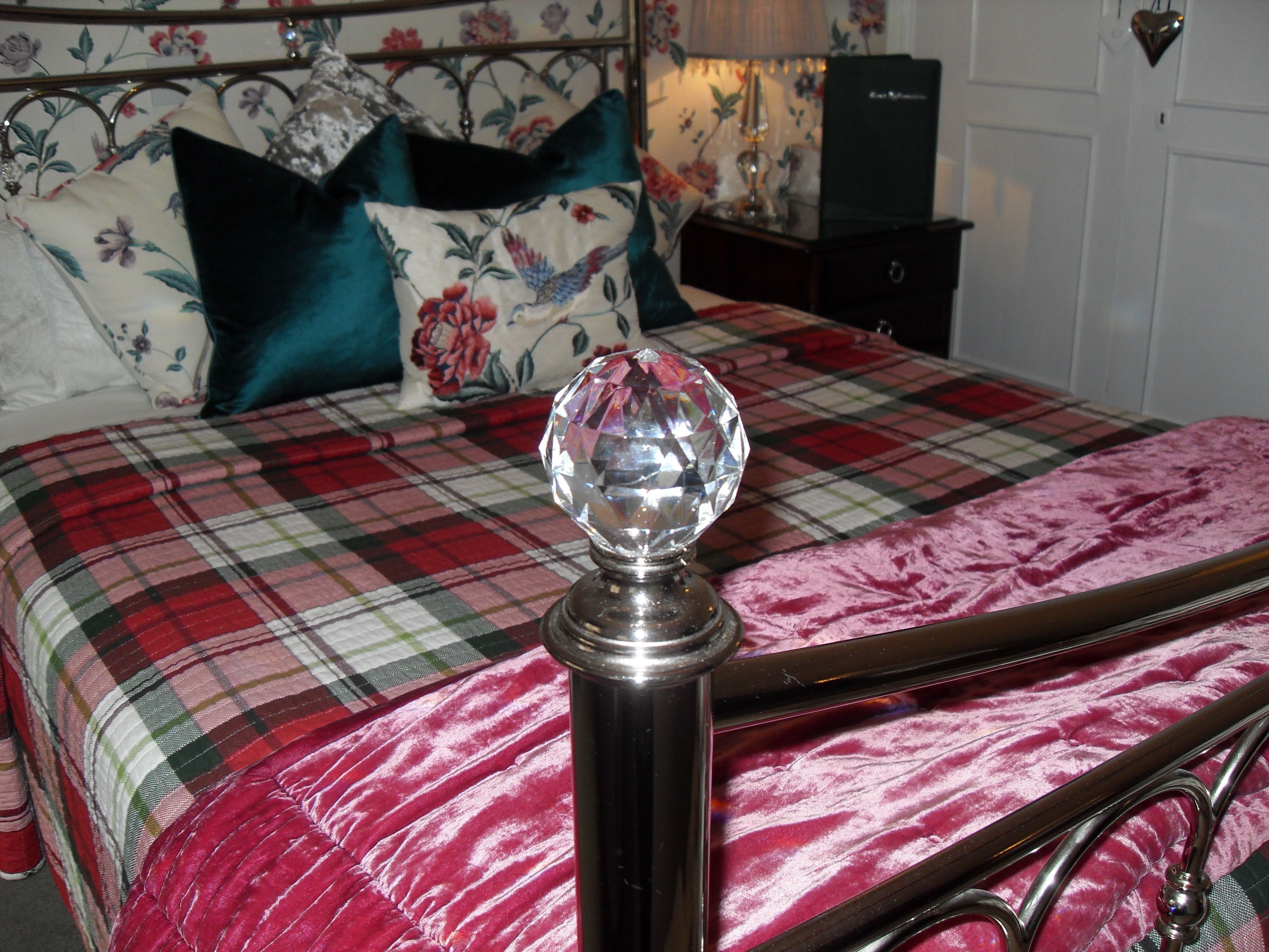 A bed with a plaid bedspread, a decorative crystal on the headboard, and floral-patterned pillows.