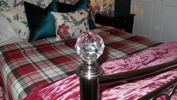 A bed with a plaid bedspread, a decorative crystal on the headboard, and floral-patterned pillows.
