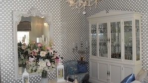 A room with a polka dot wallpaper, a chandelier, a mirror, a cabinet with glass doors, and a floral arrangement. - Jessop House (Tewkesbury)