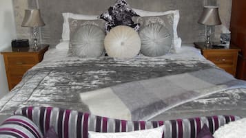 A neatly made bed with a grey and white patterned bedspread, two bedside tables with lamps, and striped pillows.