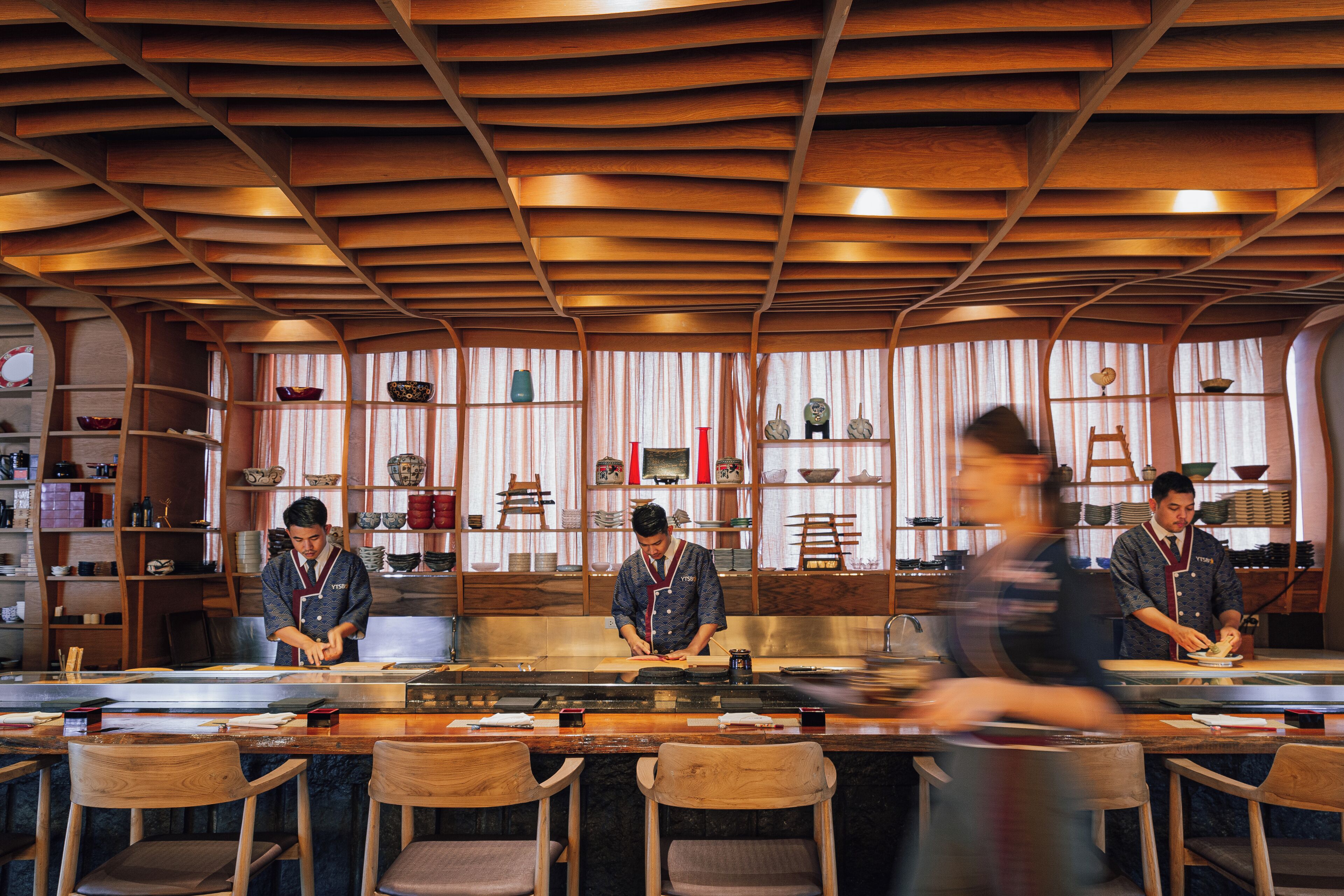 A restaurant with a wooden ceiling and bar seating.