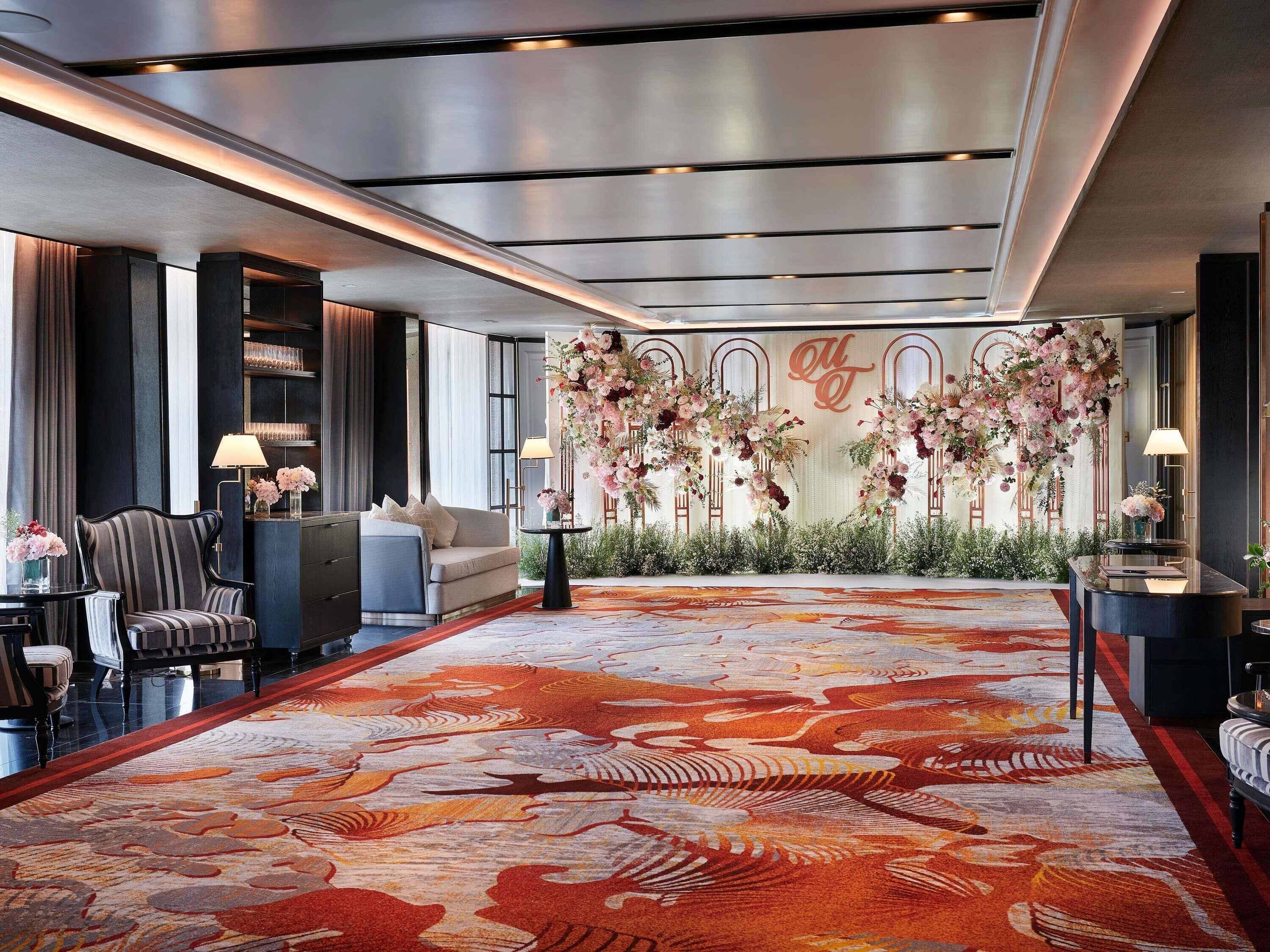 A hotel lobby with a large floral arrangement, a patterned carpet, and a seating area with a sofa and armchairs.