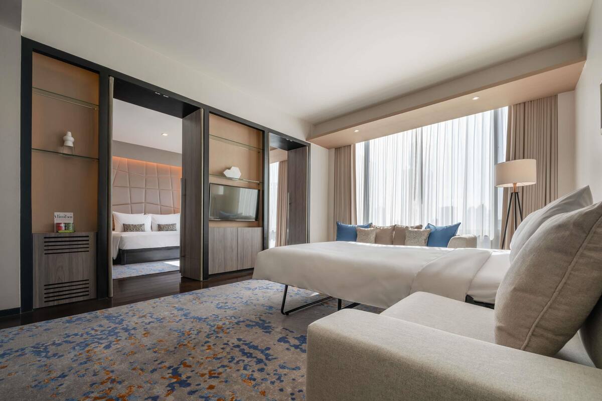 Une chambre d’hôtel moderne avec un grand lit, un canapé, une télévision et une fenêtre avec des rideaux.