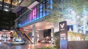 Moderne hotelentree met een zichtbare trap, een bord dat de hoofdingang aangeeft, en een parkeerplaats met auto's.