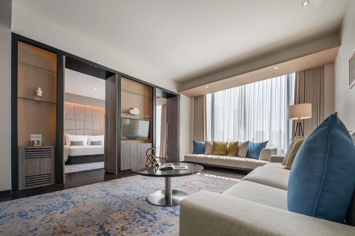 Ein modernes Hotelzimmer mit einer Couch, einem Couchtisch, einem Fernseher und einem großen Fenster mit Vorhängen.