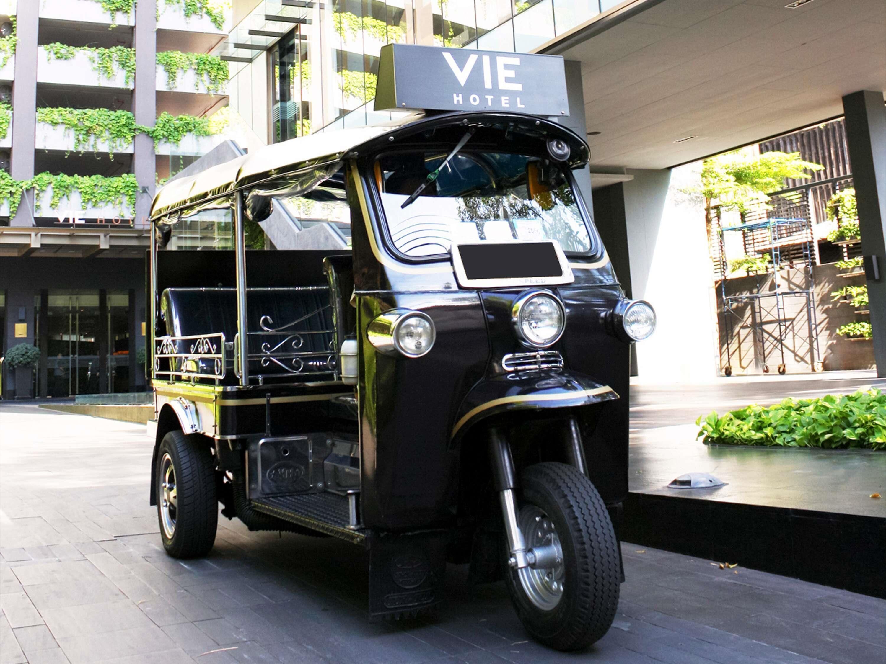 A vintage black tuk-tuk parked in front of a building with a sign that reads 'VIE HOTEL.'