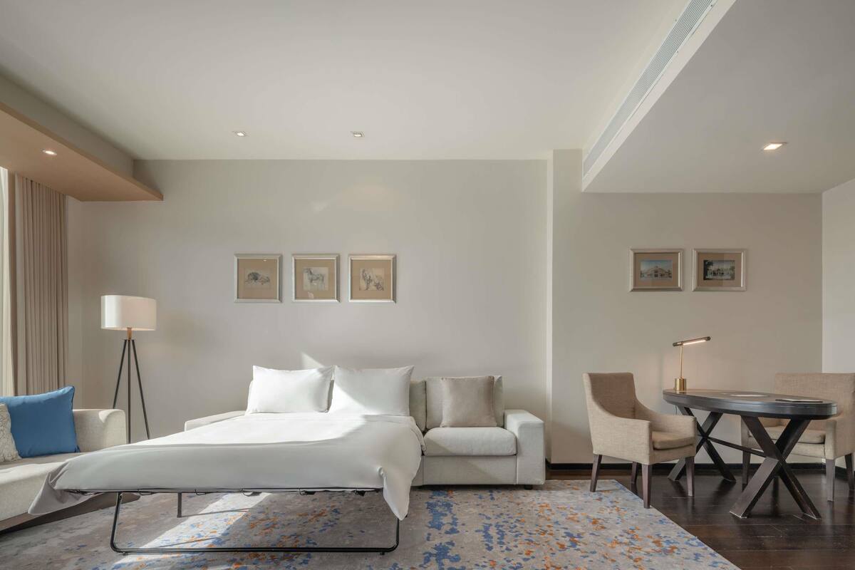 Une chambre d’hôtel comprenant un lit, un canapé, une chaise, une petite table et des œuvres d’art accrochées aux murs.