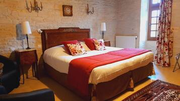 A traditional room with a brick wall, a wooden bed with red and white bedding, two bedside tables with lamps, a chair, and a patterned rug.