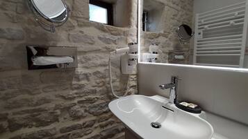 A bathroom with a stone wall, a white sink, a mirror, and a towel dispenser.