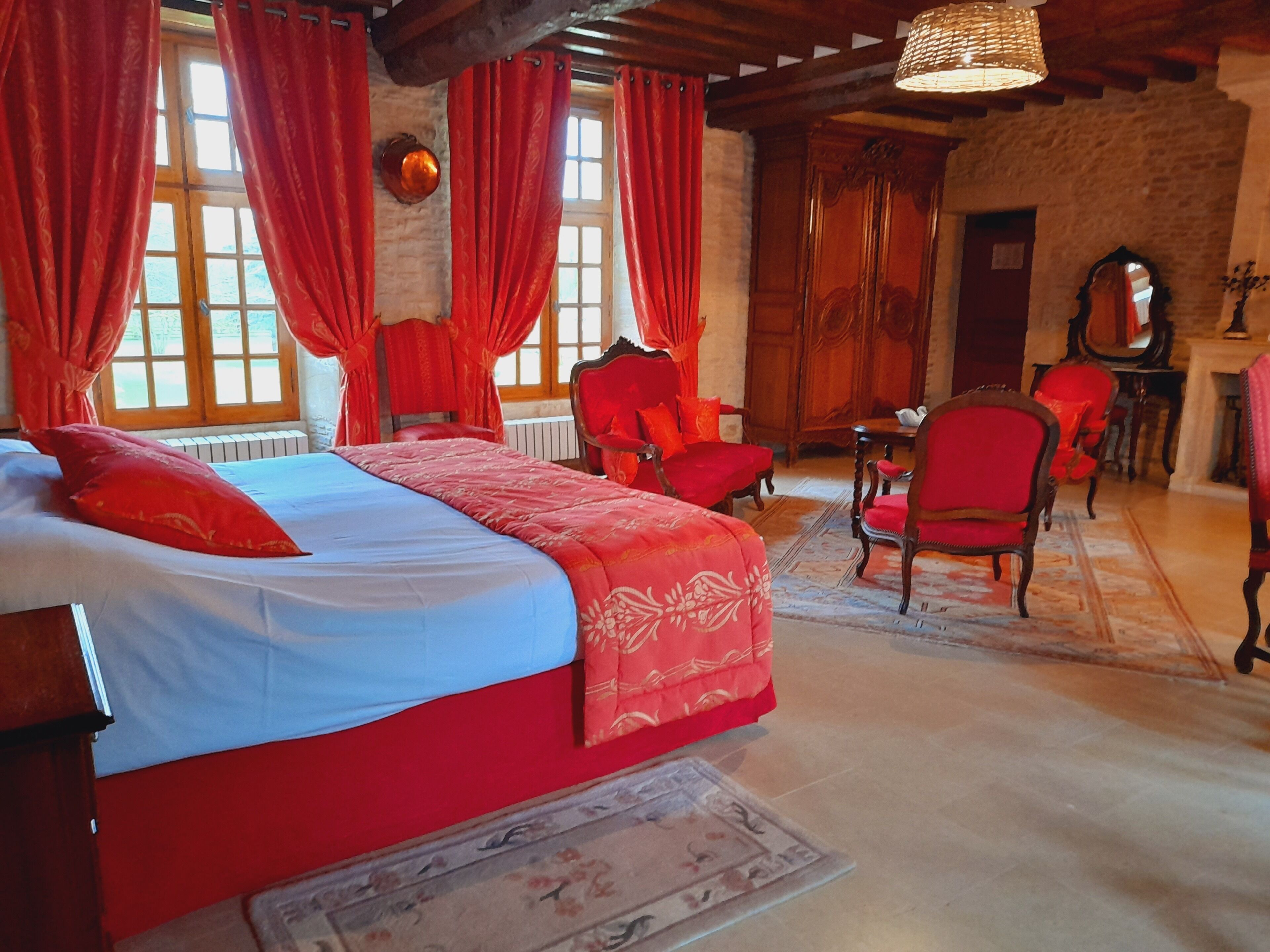 A bedroom with a large bed, red curtains, and a wooden ceiling.