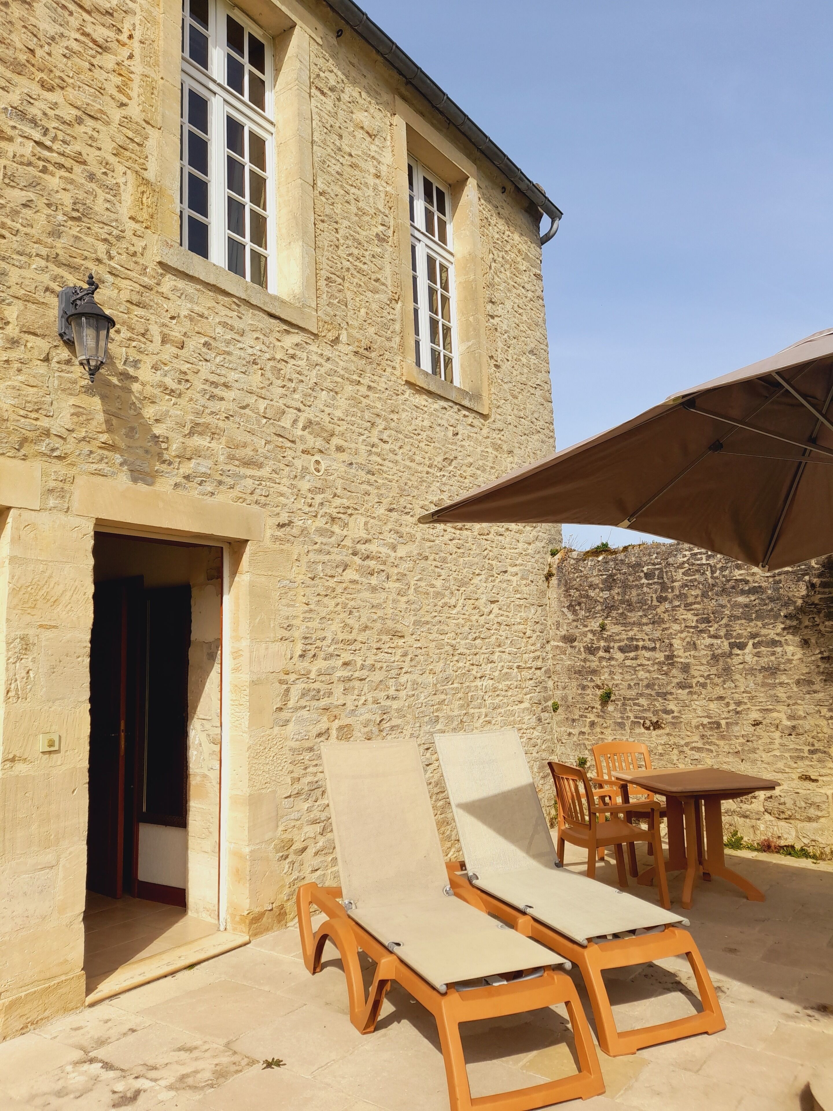A stone building with a door, windows, and a table with chairs outside.