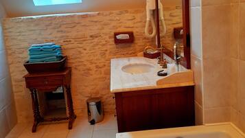 A bathroom with a skylight, a sink, a mirror, a bathtub, a wooden stool, and a trash can.