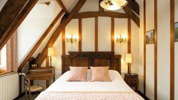 A bedroom with a large bed, wooden headboard, two bedside lamps, a desk with a chair, and a window with curtains.