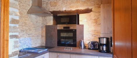 A kitchen with a stone wall, wooden cabinets, a built-in oven, and a coffee maker.