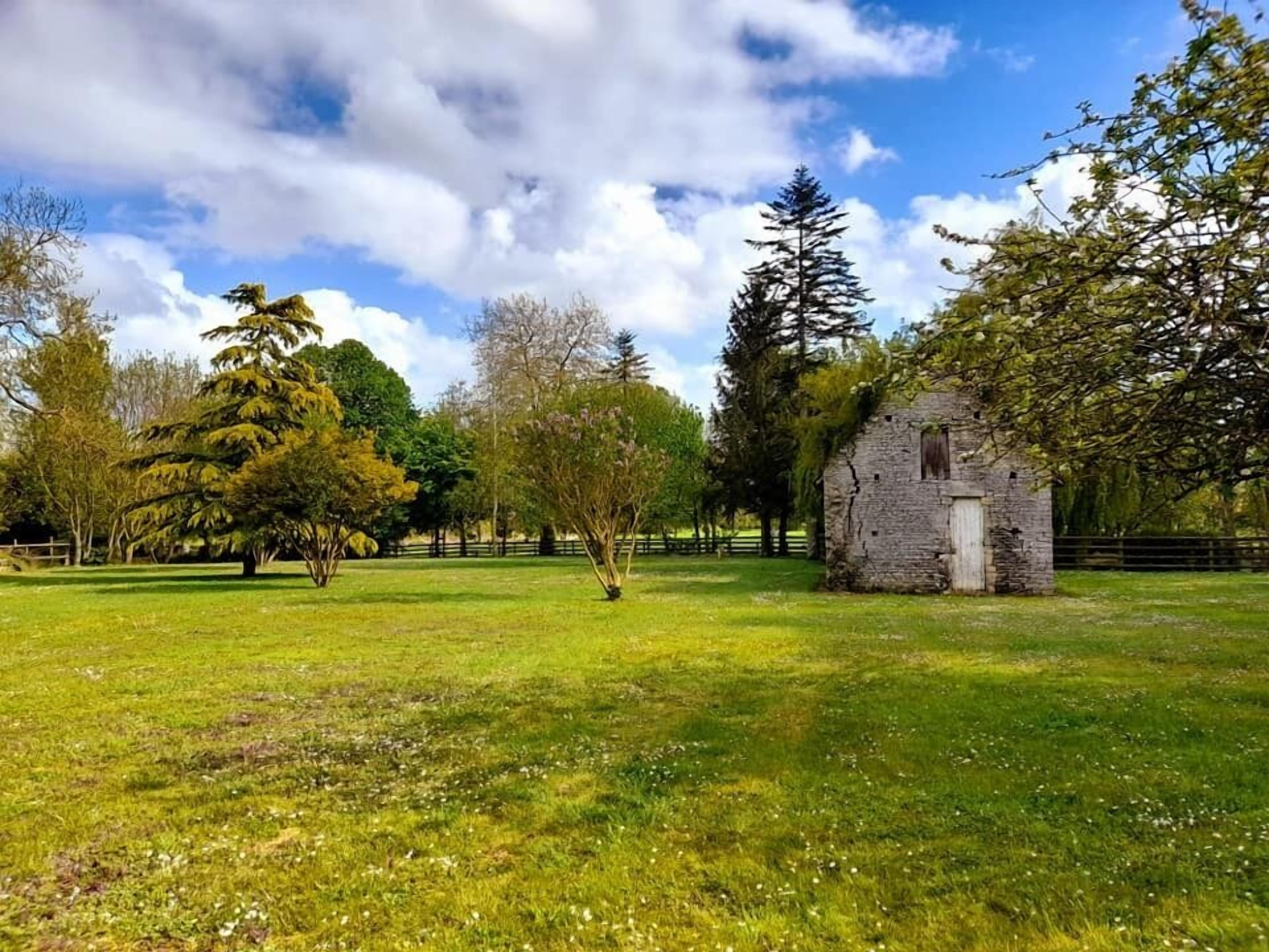 A grassy field with a stone building and trees.