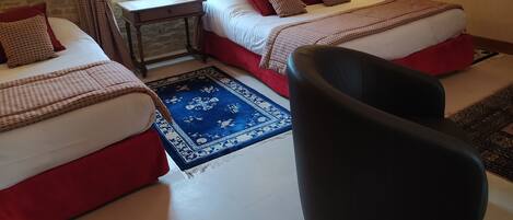 A room with two beds, a small table, a chair, and a window with curtains.