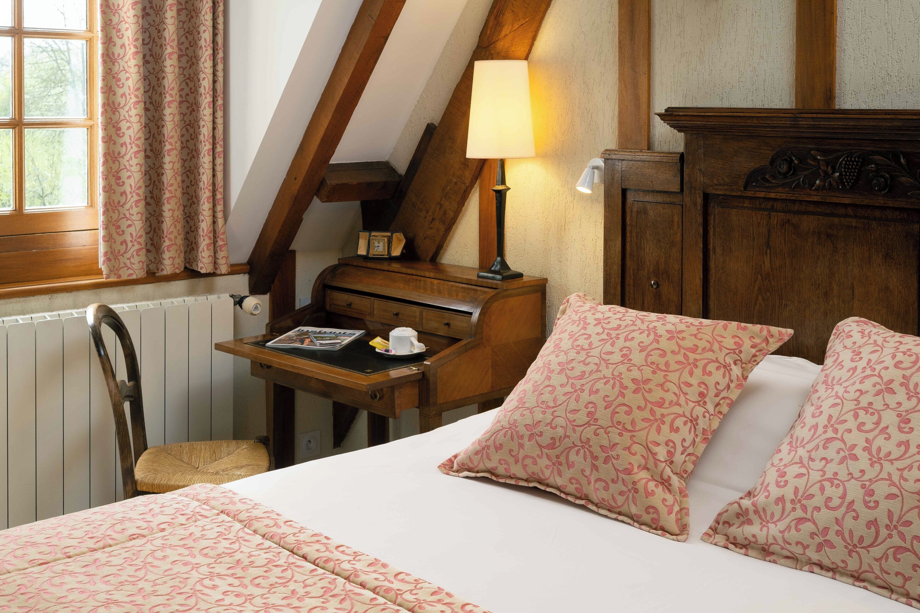 A bedroom with a bed, a desk with a lamp, a chair, and a radiator.