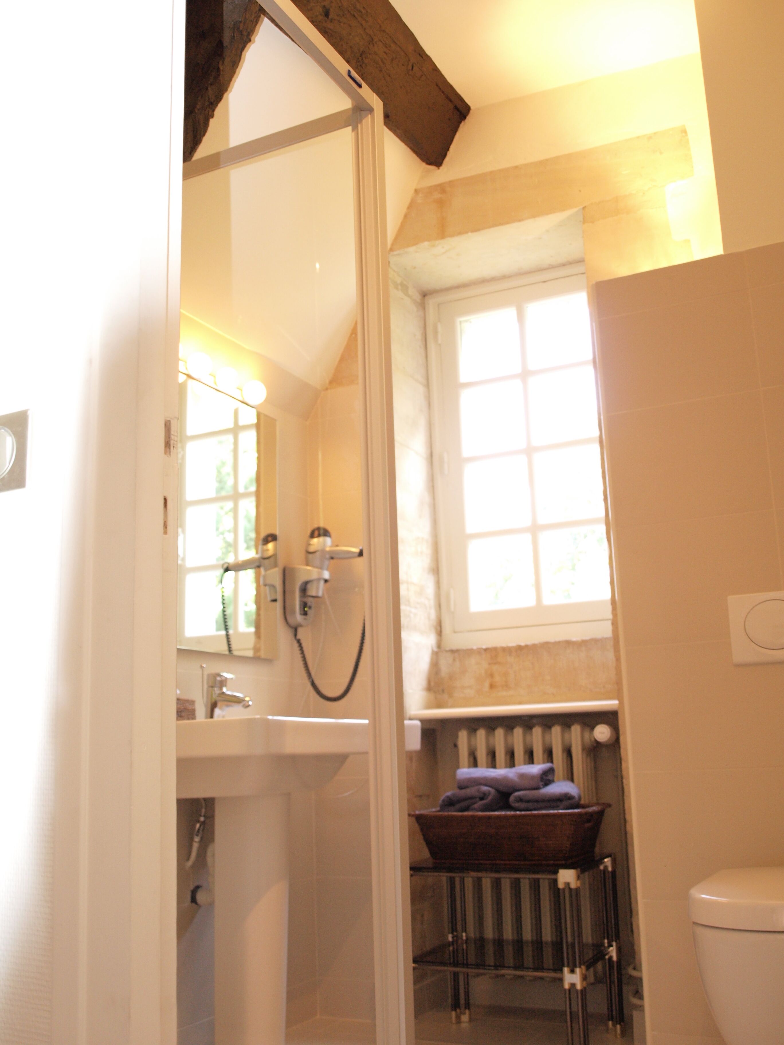 A bathroom with a shower, a sink, a window, and a radiator.