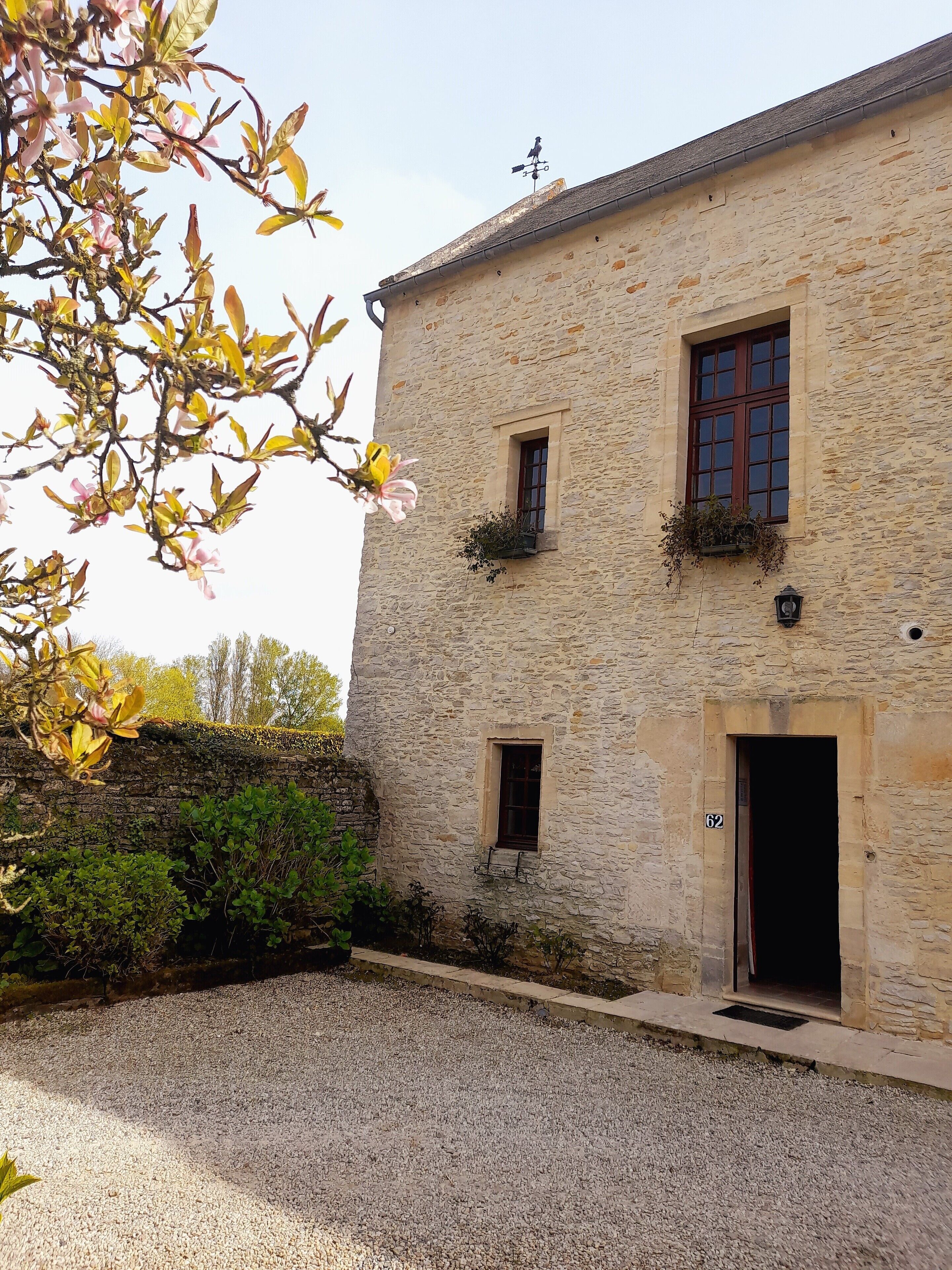 Un bâtiment en pierre avec deux fenêtres, une porte et un petit balcon agrémenté de plantes.