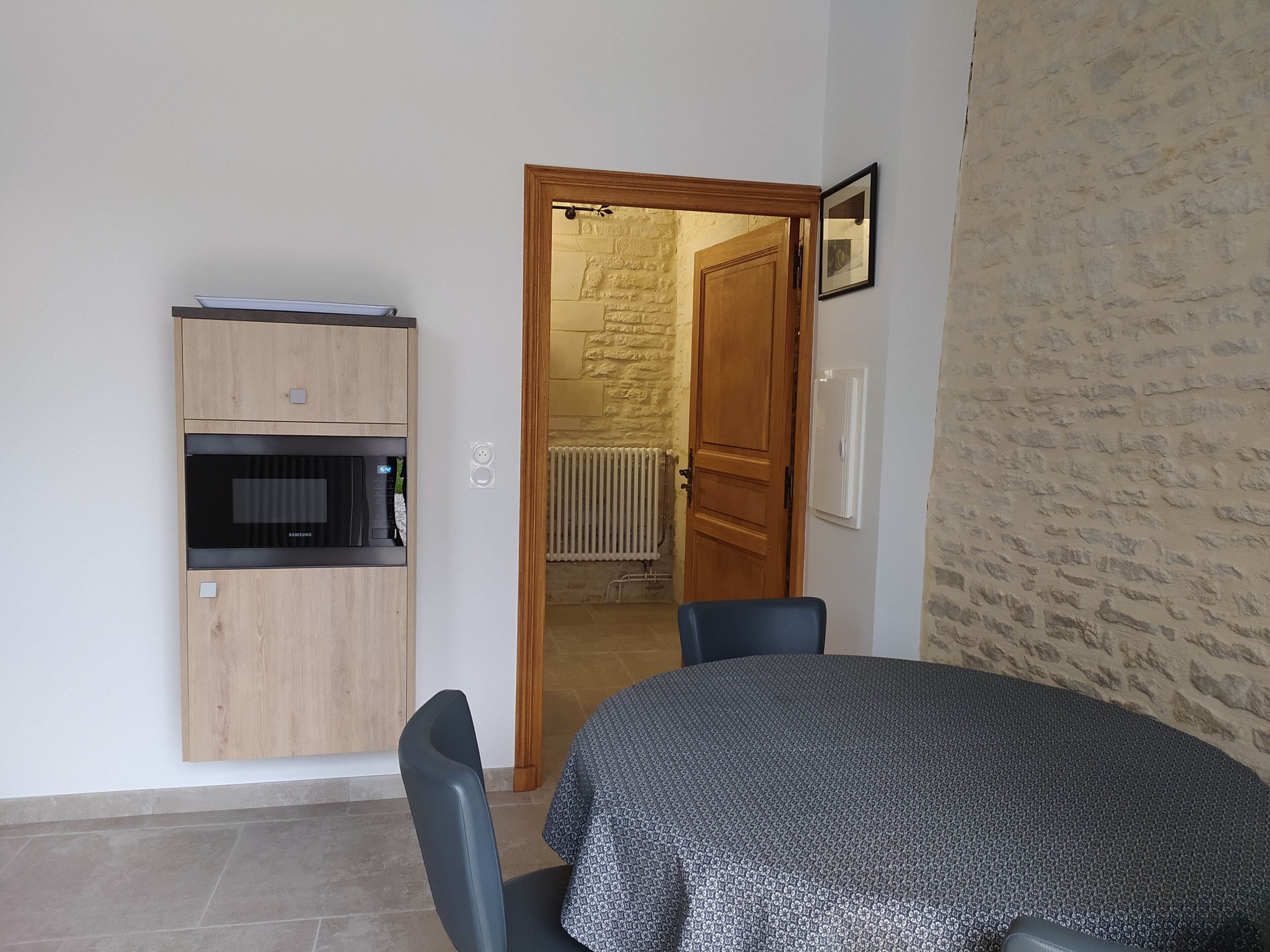 A compact kitchen with a built-in microwave and oven, a dining area with a table and chairs, and a doorway leading to a room with a stone wall.