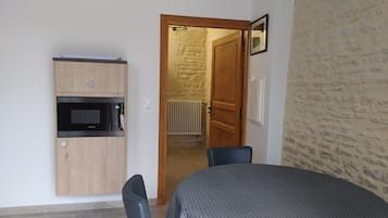 A compact kitchen with a built-in microwave and oven, a dining area with a table and chairs, and a doorway leading to a room with a stone wall.