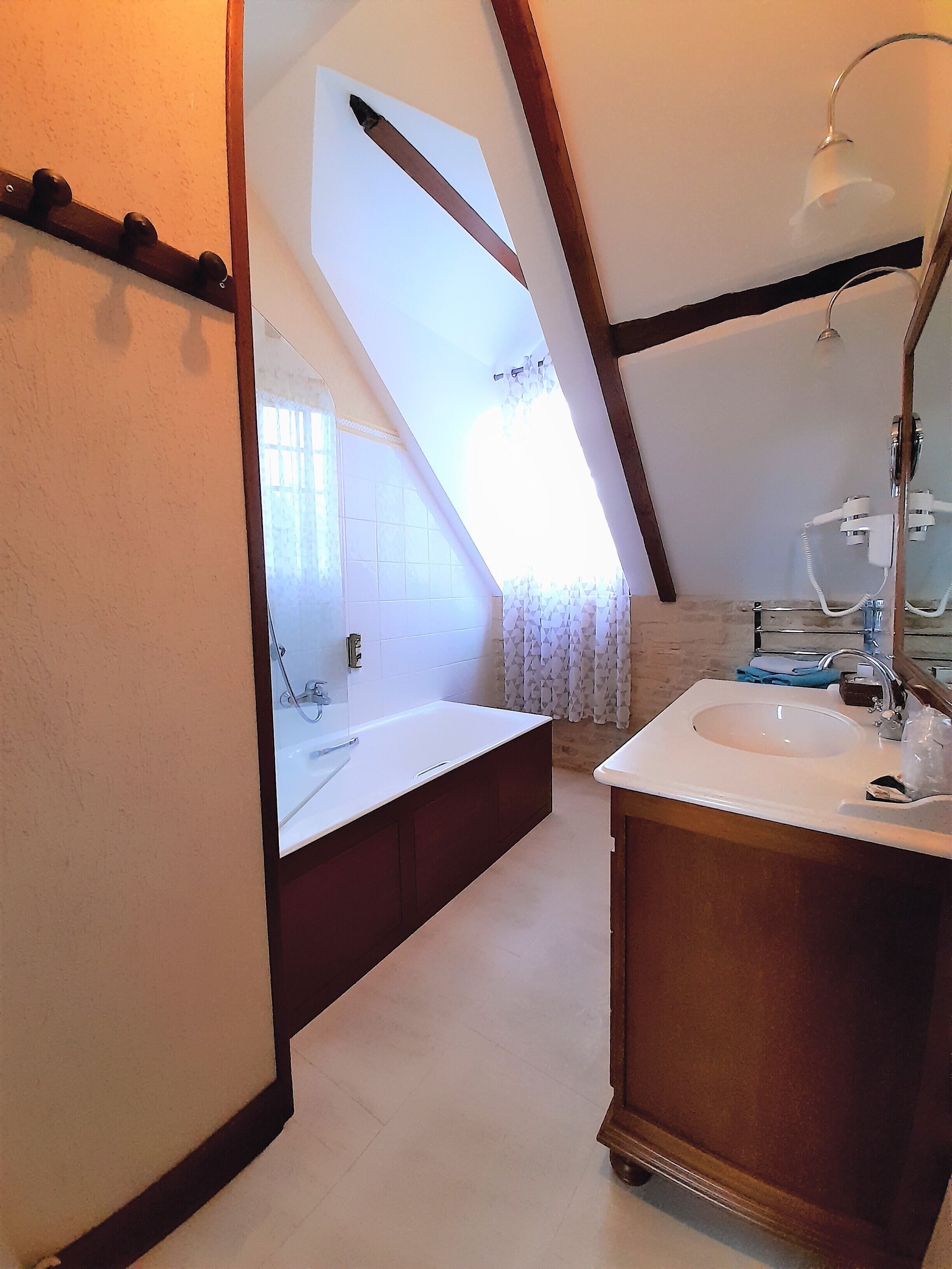 Un baño con bañera, lavamanos y ducha. Hay una ventana con cortinas y un perchero para toallas.