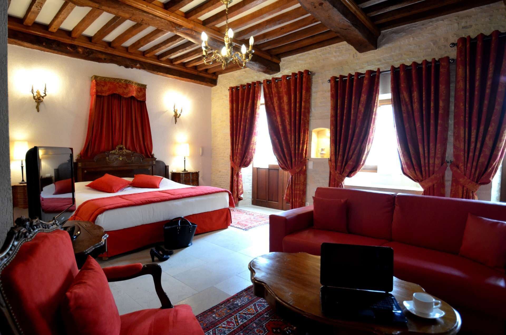 A hotel room with a bed, a sofa, a laptop on a table, and a red carpet.