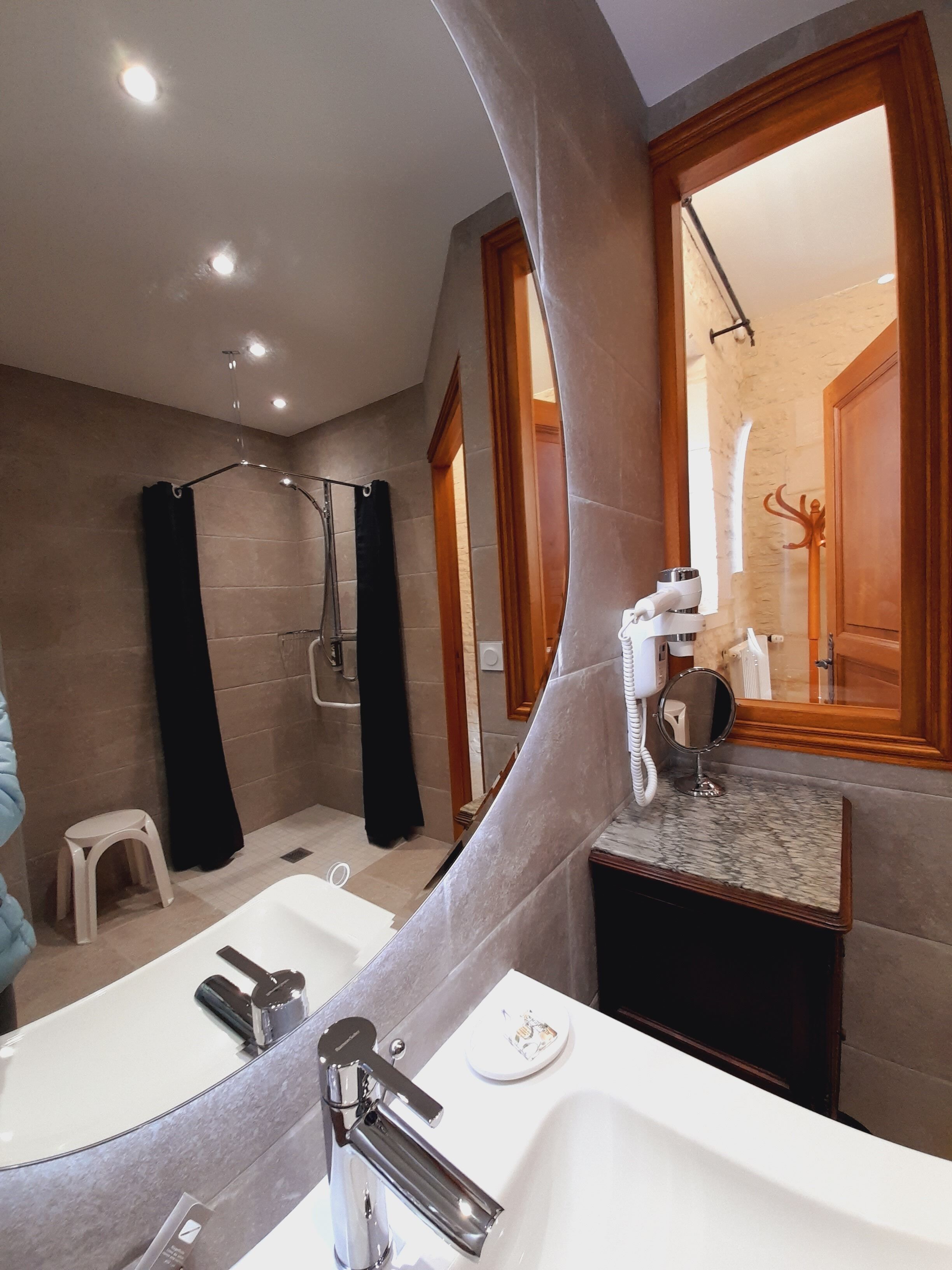 A modern bathroom with a large mirror, a shower, and a vanity with a sink.
