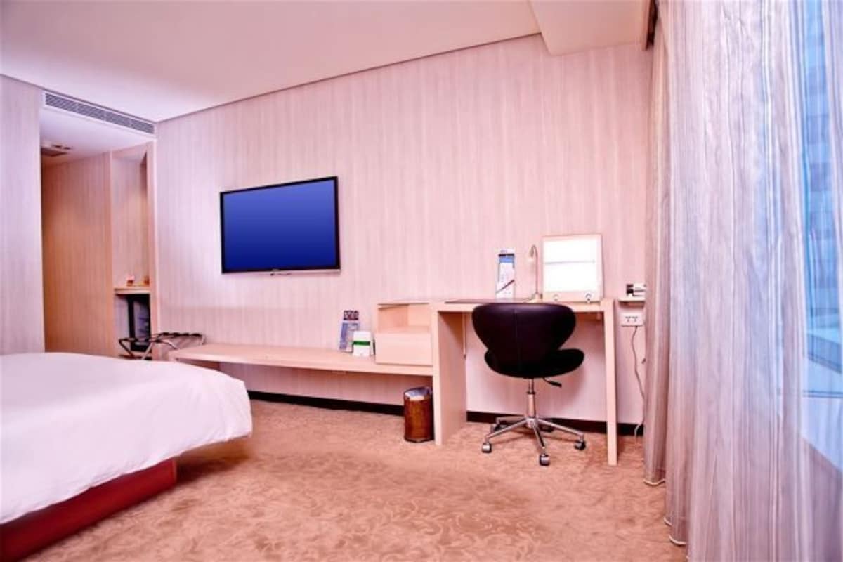 Habitación de hotel con una cama, un escritorio con computadora, una silla y un televisor montado en la pared.