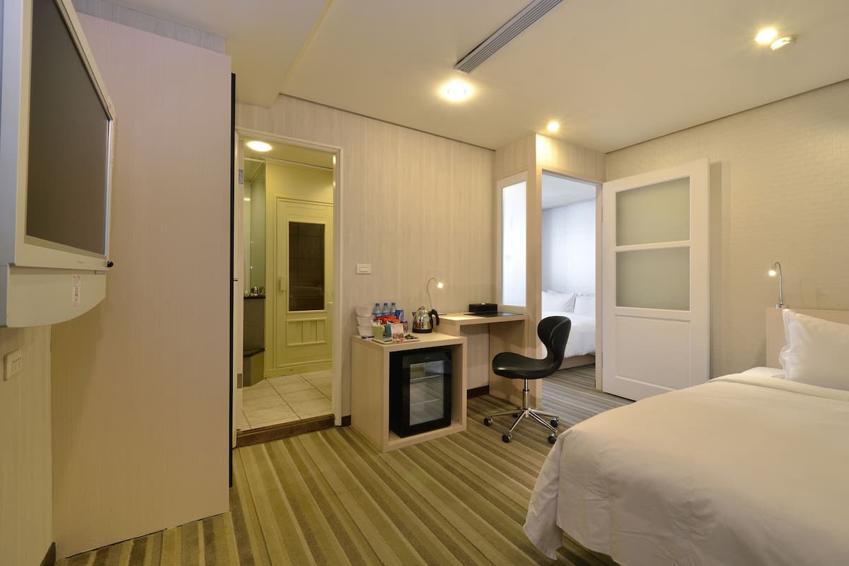 A hotel room with a bed, a desk with a chair, a mini-fridge, and a mirror.