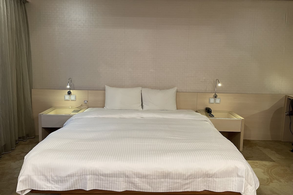 A hotel room with a large bed, two bedside tables with lamps, a power outlet, and a telephone on the right side.