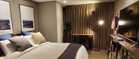 A hotel room with a large bed, a desk with a computer, a TV, and a plant.