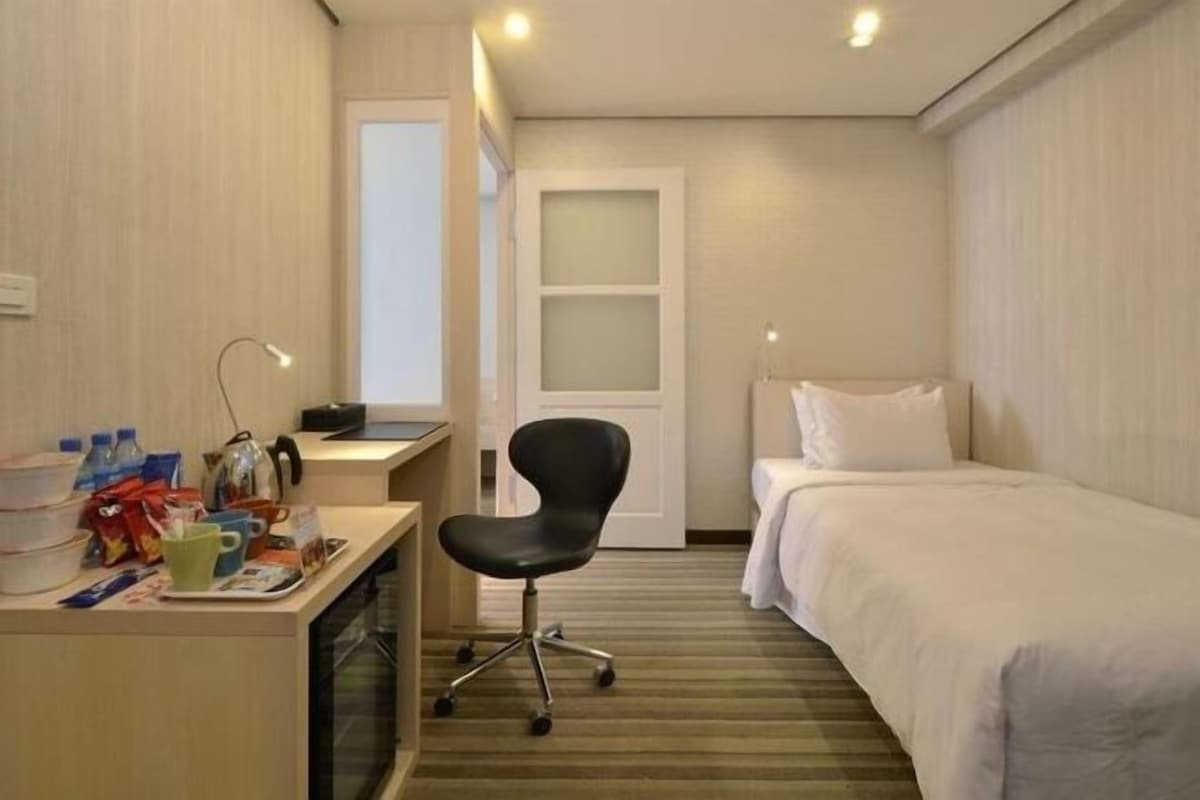 Una habitación de hotel con una cama, un escritorio con una silla, una ventana y una puerta.
