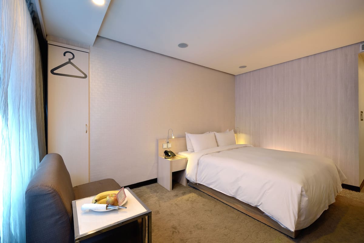 A hotel room with a bed, bedside table, and a hanging coat rack.