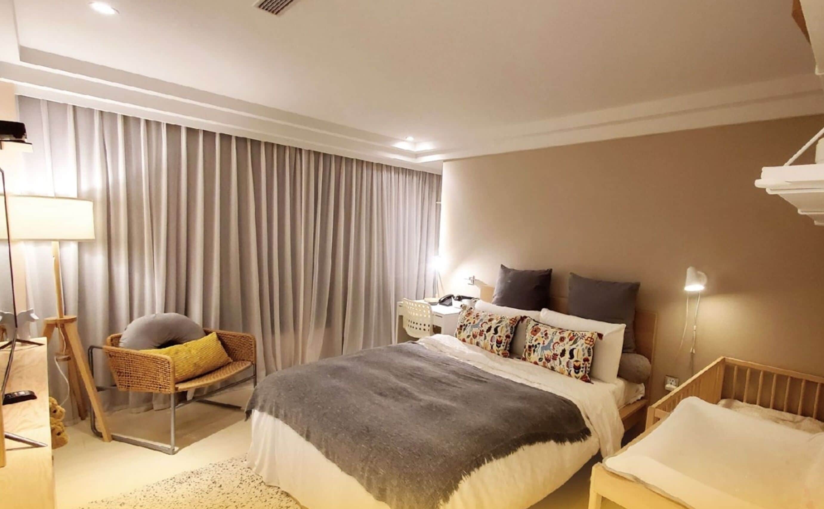 A modern hotel room with a large bed, a bedside table, a chair, a desk, and a lamp.