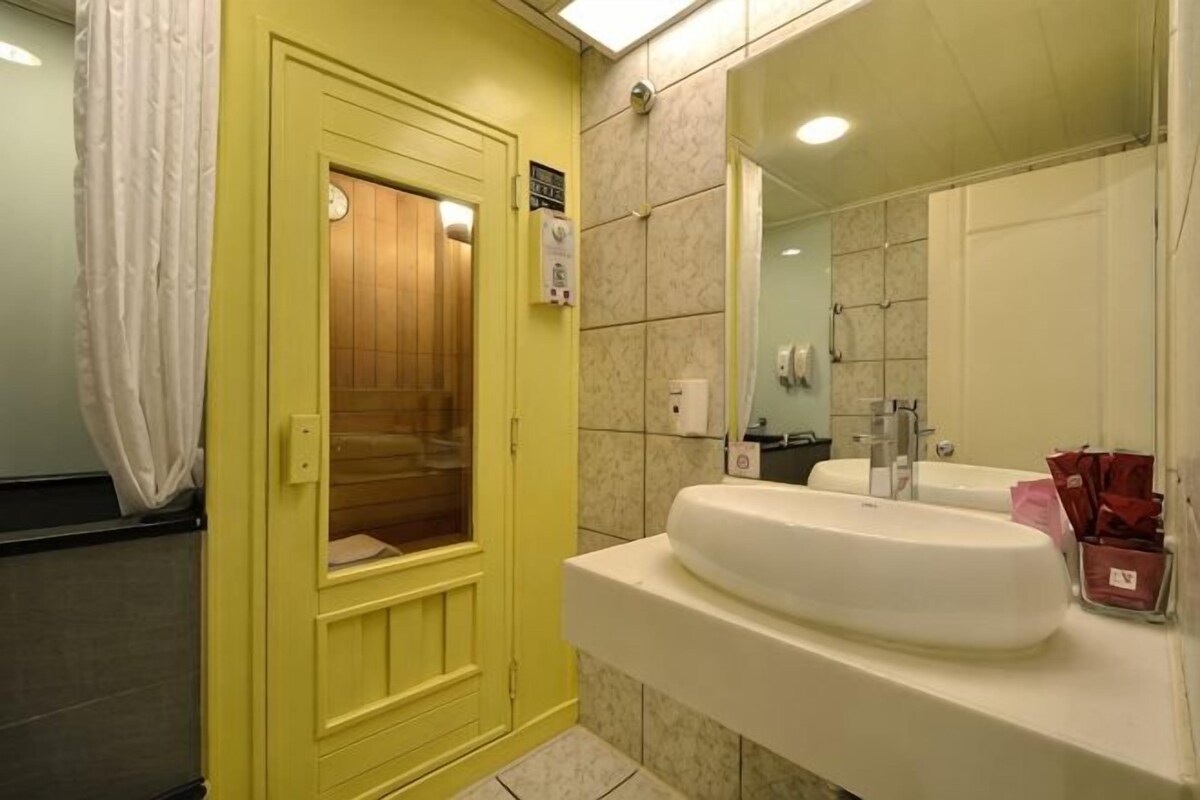 Un baño con puerta amarilla, lavamanos blanco, espejo y zona de ducha.