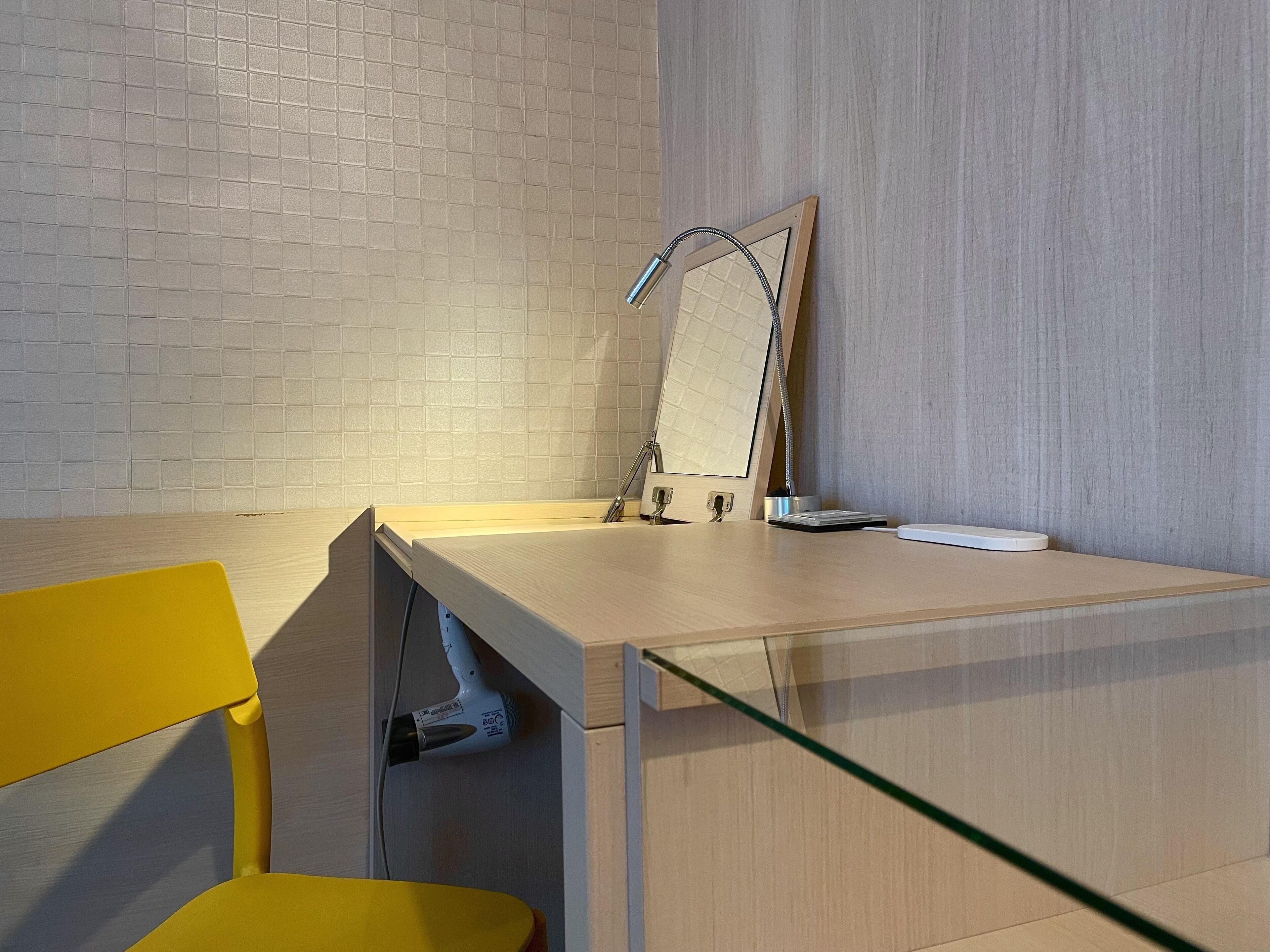 A modern bathroom with a tiled wall, a wooden vanity, a mirror, and a yellow chair.