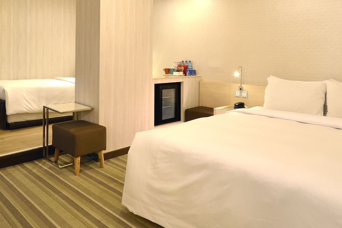 A hotel room with a large bed, a small table, a chair, a desk, and a mirror.