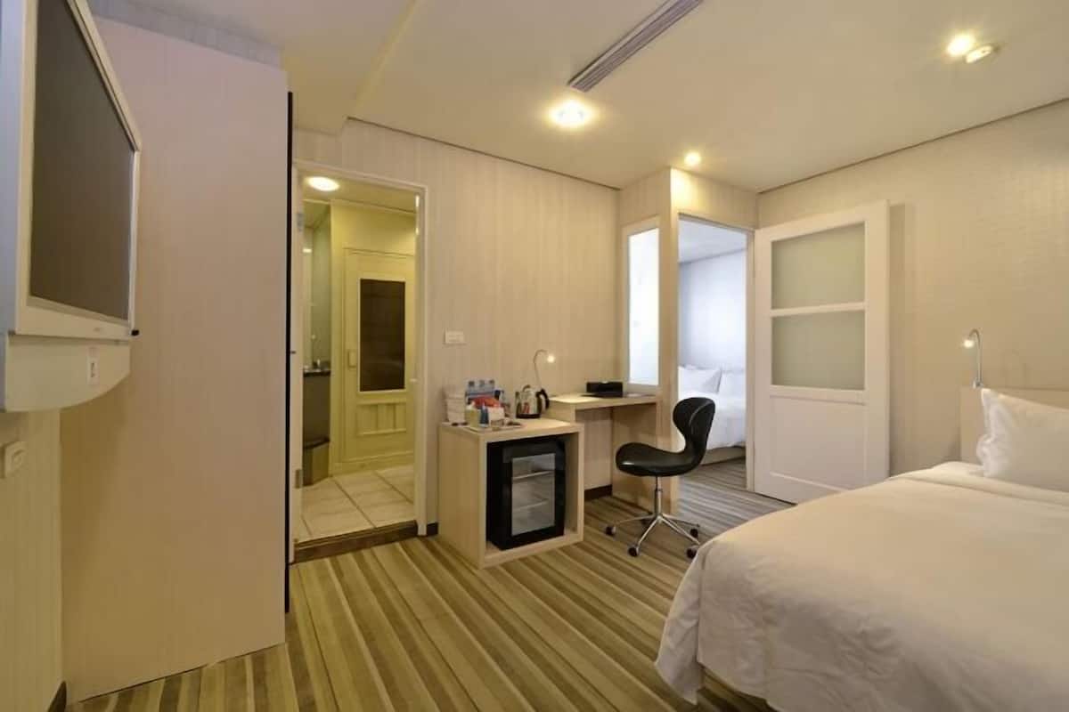 A hotel room with a bed, desk, chair, and a small kitchenette.